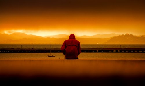 Person Wearing Red Hoodie Sitting In Front Of Body Of Water photo