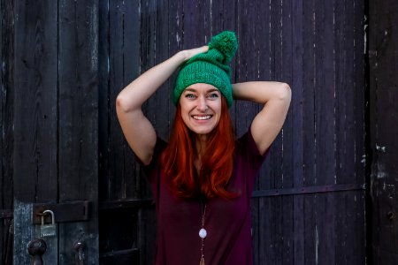 Woman In Green Bobble Cap And Purple T-shirt Posing Near Black Wooden Fence photo