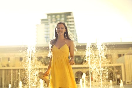 Woman Wears Yellow Spaghetti Strap Dress Stands Near Water Fountain photo