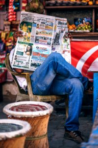 Man Sitting On Plastic Armchair Reading Newspaper