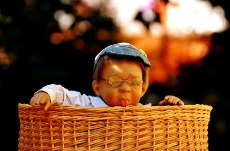 Baby Doll Wearing Eye Glasses Inside The Brown Wicker Basket photo