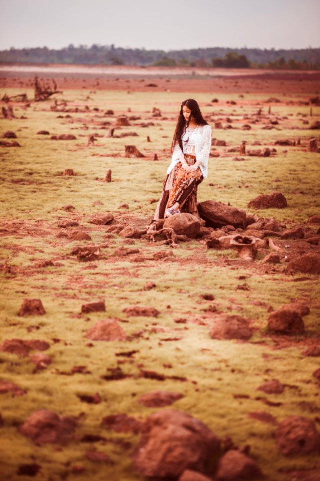 Woman In White Cardigan And Brown Pants Sitting On Stump During Daytime