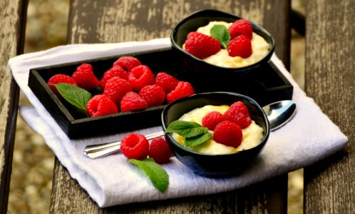 Raspberries On Black Rectangular Tray Beside Black Round Bowl With 3 Raspberries Beside Silver Spoon On Top Of White Textile photo