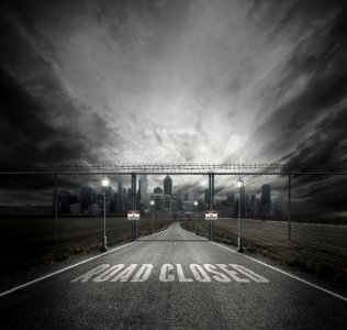 Grayscale Photo Of Road Closed On Roadway With Gray Fence Gate In Front Of City photo