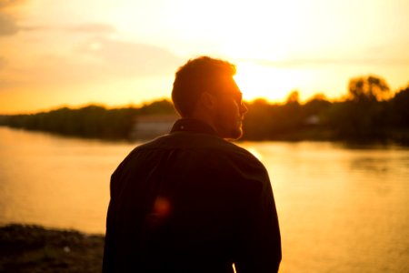 Man Sitting Near Large Body Of Water Under Clear Sky During Sunset photo