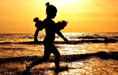 Silhouette Of Girl Running On The Seashore During Golden Hour photo