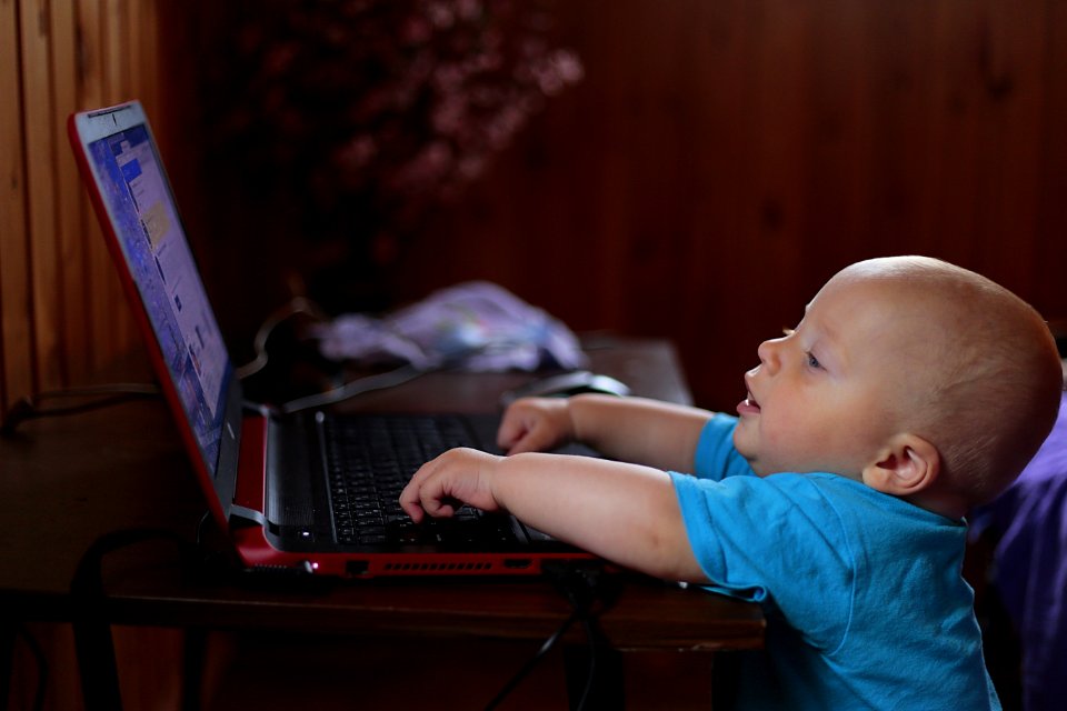Boy Wearing Blue T Shirt Using Black Laptop Computer In A Dim Lighted Scenario