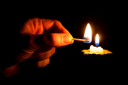 Person Holding Match Stick With Fire In Front Of Candle With Fire photo