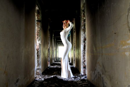 Woman In White Bodycon Maxi Dress Posting In Between White Concrete Wall photo
