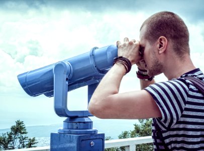 Person In White And Gray Stripes Crew Neck T Shit Using Telescope Near White Metal Handrails Under White Clouds During Daytime