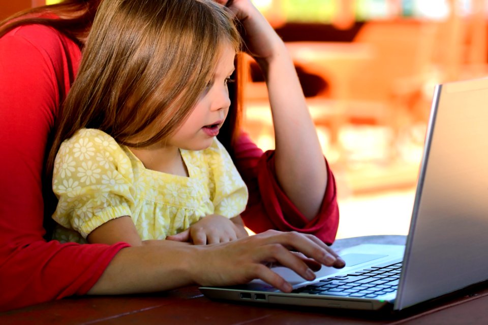 Brunette Woman In Red With Girl In Yellow On Lap Before Laptop