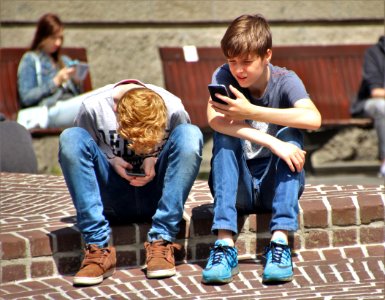 2 Boy Sitting On Brown Floor While Using Their Smartphone Near Woman Siiting On Bench Using Smartphone During Daytime photo