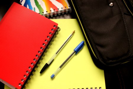 Black And Blue Pens Beside Red Covered Notebook