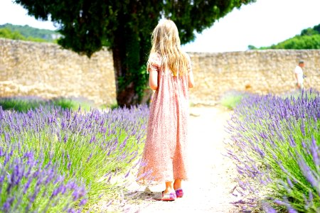 Woman Wearing Pink Maxi Dress Walking Along Unpaved Pathway With Purple Plants Nearby