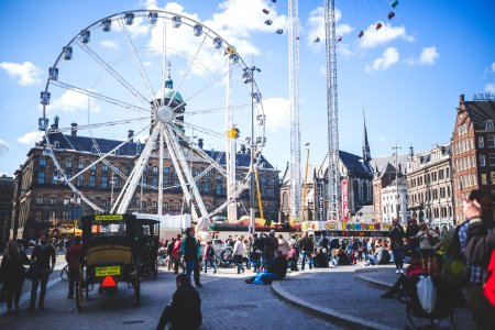 Ferris Wheel Beside Brown Buildings And People Under Blue Cloudy Sky At Daytime photo