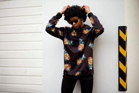 Photo Of A Woman In Pineapple Print Pullover Leaning On White Wall photo