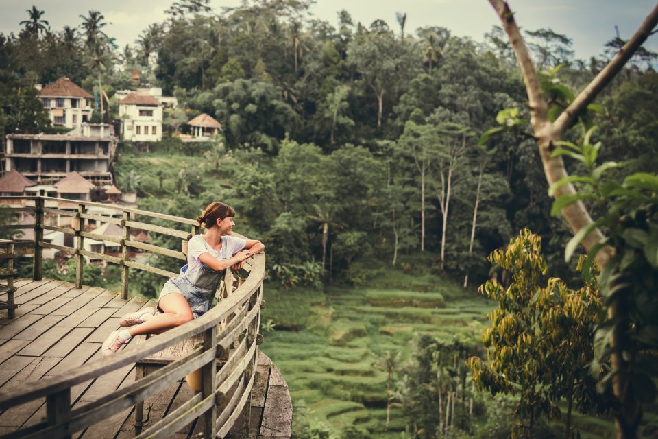 Woman Sits On Bench Overlooking Tall Trees At Daytime