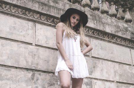Woman In White Sleeveless Dress And Hat Near Wall