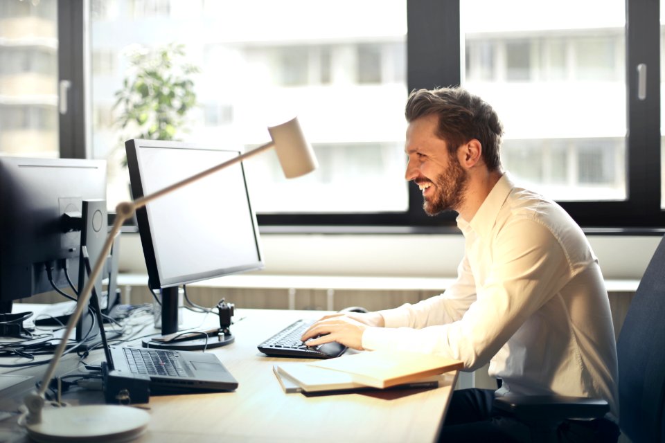 Man In White Dress Shirt Sitting On Black Rolling Chair While Facing Black Computer Set And Smiling