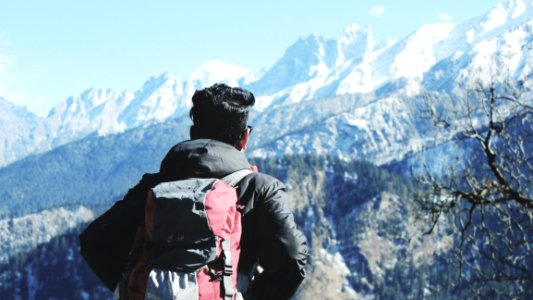 Photography Of Man In Black Hooded Jacket And Red Backpack Facing Snow Covered Mountain photo