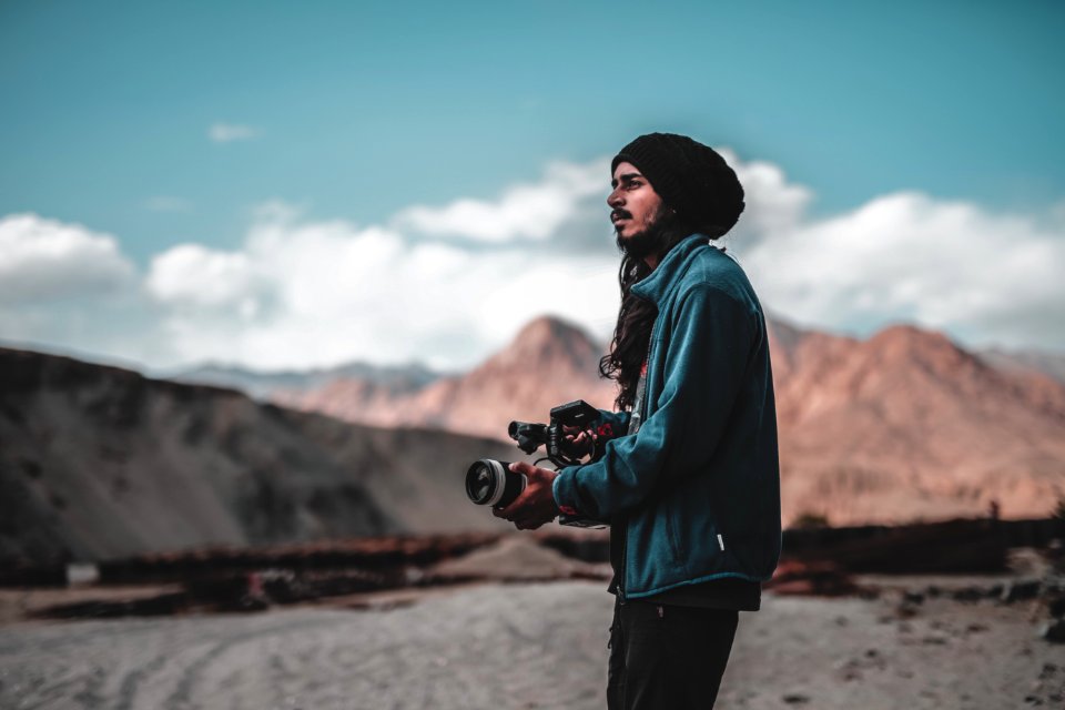 Man Wearing Jacket Holding Dslr Camera On Desert