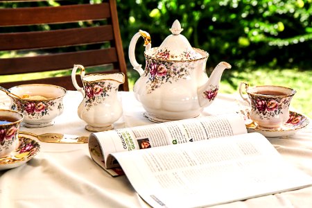 White And Pink Floral Ceramic Tea Set On White Textile Covered Table Beside White And Black Printed Book photo