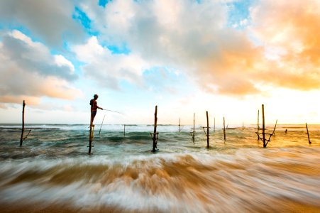 Man Standing In Wood In The Middle Of The Ocean While Fishing Under Blue And White Sky During Day Time photo