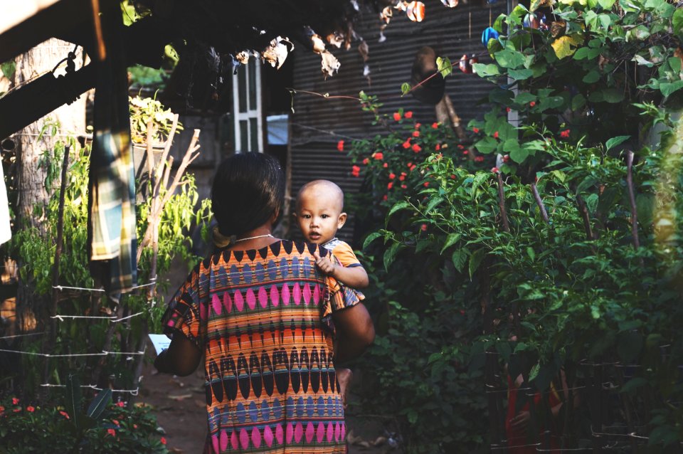 Woman In Orange Pink Aztec Dress Carrying Child In Orange Shirt