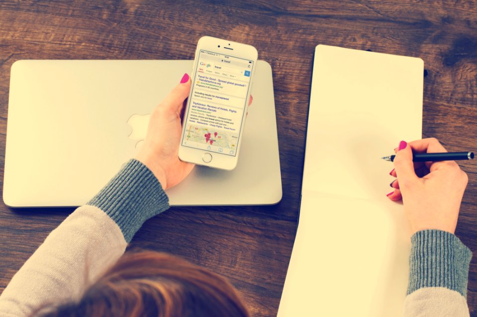 Hands Holding Cellphone And Pen On Desk