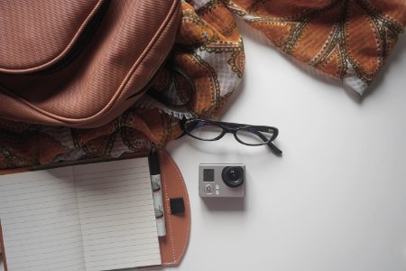 Black Eyeglasses On Top Of The Gray And Black Action Camera In The White Surface