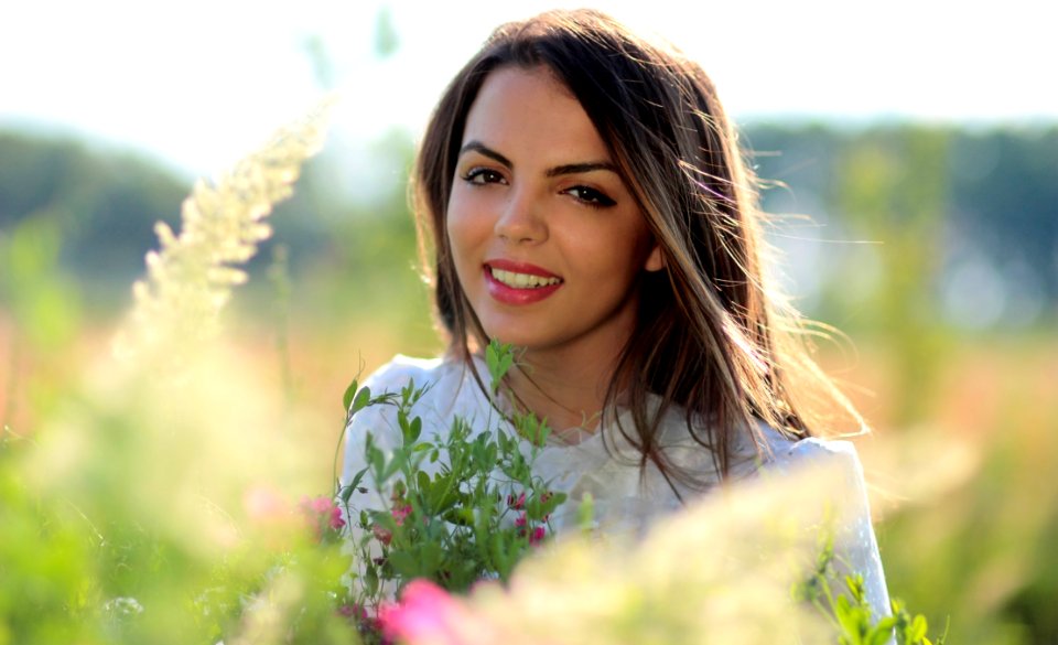 Woman In White Crew Neck Shirt Smiling And Surround With Flowers And Plants During Daytime