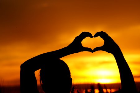 Silhouette Woman Hand Holding Heart Shape Against Orange Sky photo