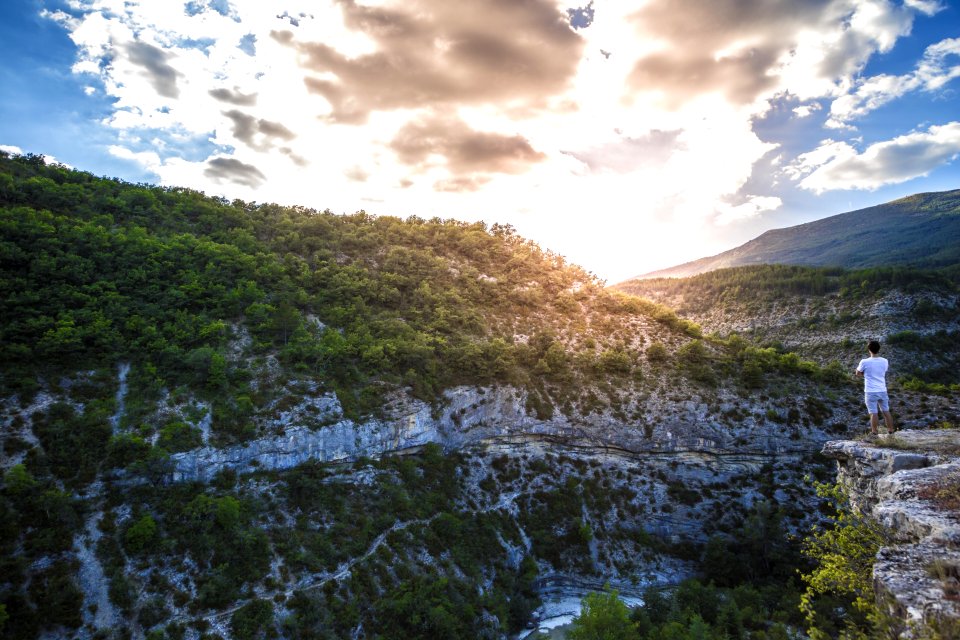 Man In White Shirt Standing On Top Of Mountain Cliff Under Cumulus Clouds