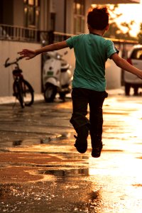 Boy In Green T Shirt Running On Wet Road During Daytime
