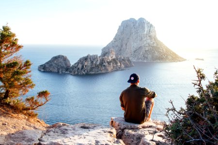 Rear View Of Man Sitting On Rock By Sea