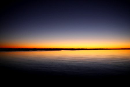 Silhouette Of Calm Sea Under Blue And Orange Clear Sky During Sunset photo