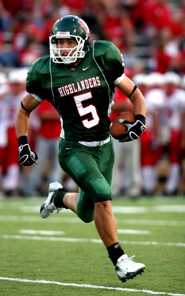 Man Wearing Green American Football Jersey Holding The Ball While Running On The Field