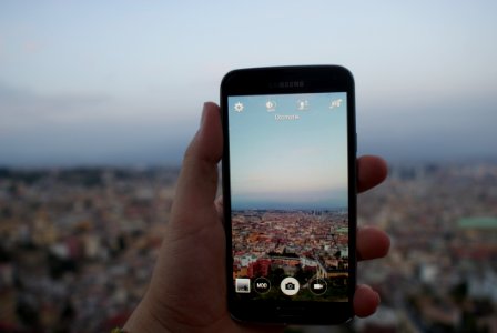 Person Holding A Black Samsung Galaxy Android Smartphone Taking A Picture Of Cityscape Over Blue And White Sky During Daytime photo