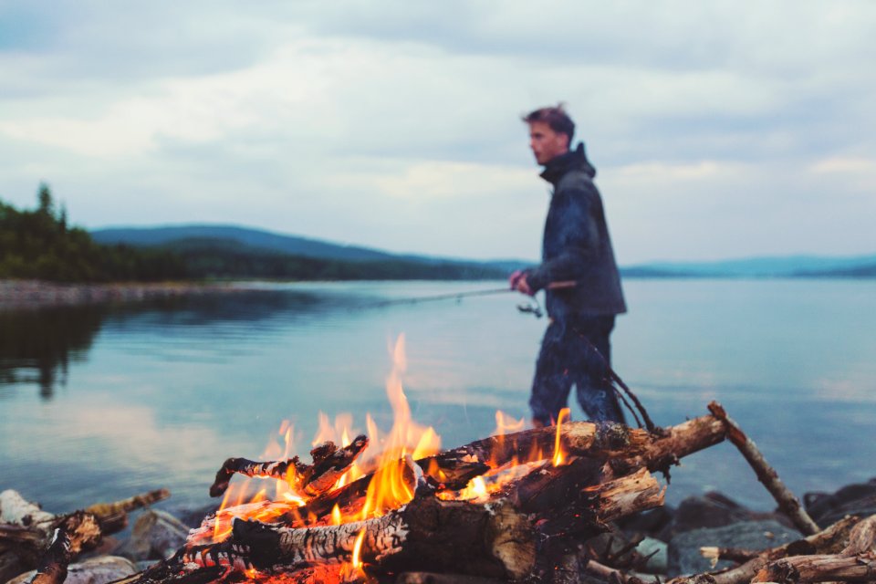 Man Holding Fishing Rod On Lake By Campfire