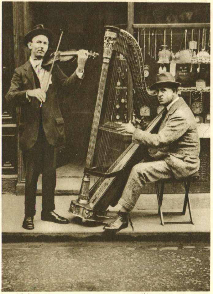 The Strains Of The Itinerant Harpist Come Through The Din Of Traffic