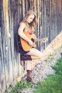 Woman Playing Guitar While Leaning On Wood During Daytime