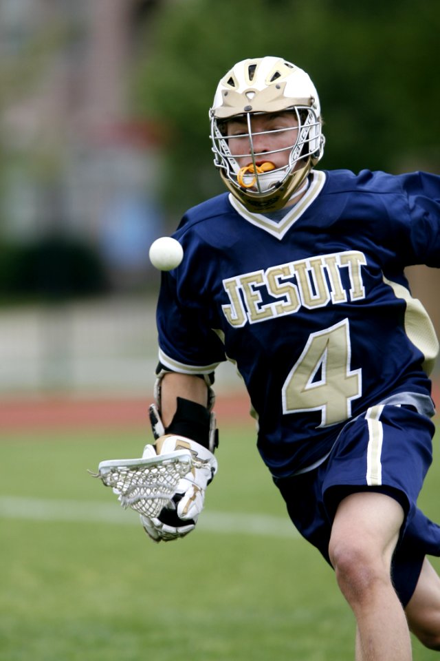 Man Holding Lacrosse Stick Running On Field During Daytime