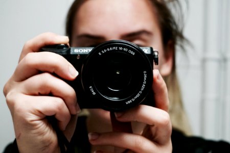 Woman Holding Black Sony Dslr Camera Taking A Photo Of Herself At Mirror