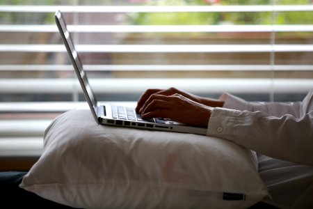 Person Wearing White Dress Shirt Using Silver Laptop On Top Of White Throw Pillow photo