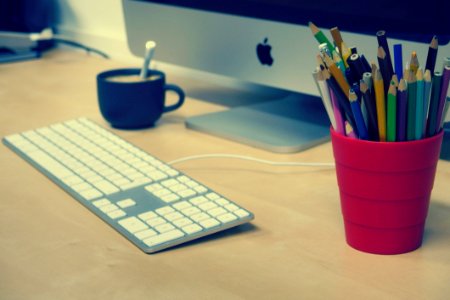 Blue Green And Black Colored Pencils On Red Plastic Cup Beside Silver Imac photo