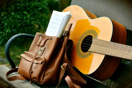 Brown Acoustic Guitar Beside Brown Leather Bucket Backpack On Brown Wooden Bench photo