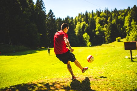 Man In Red T Shirt Playing Soccer During Daytime