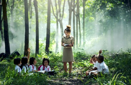 Woman In Gray Long Sleeve Dress Standing Between Childrens Near Woods And Grass photo