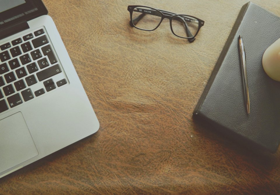 Macbook Pro Beside Black Framed Eyeglasses On Brown Wooden Surface