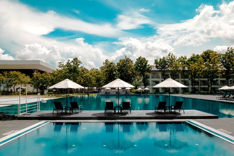 Black Outdoor Lounge Chair In Between Blue Swimming Pool Under White Cloudy Blue Sky